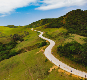 Geschwungene Straße führt durch grüne Hügel und weite Landschaft mit blauem Himmel auf den abgelegenen Batanes-Inseln.