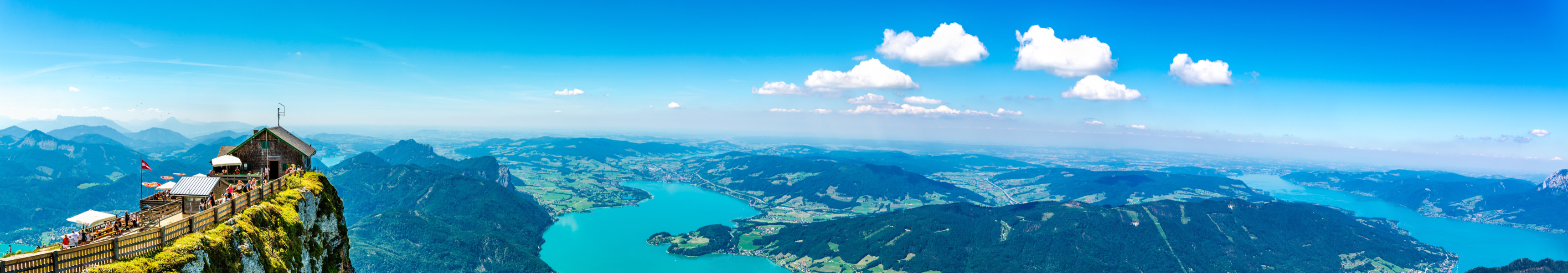 Blick vom Schafberg in Österreich auf das Salzkammergut mit einem Panorama von Bergen, Seen und grünen Wäldern an einem klaren, sonnigen Tag.
