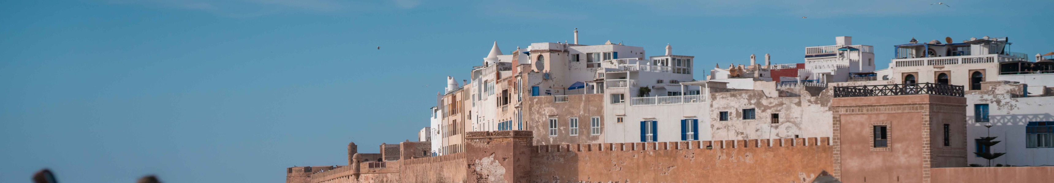 Blick auf die historische Altstadt von Essaouira in Marokko mit Stadtmauer, weißen Häusern und Fischerbooten im Vordergrund.