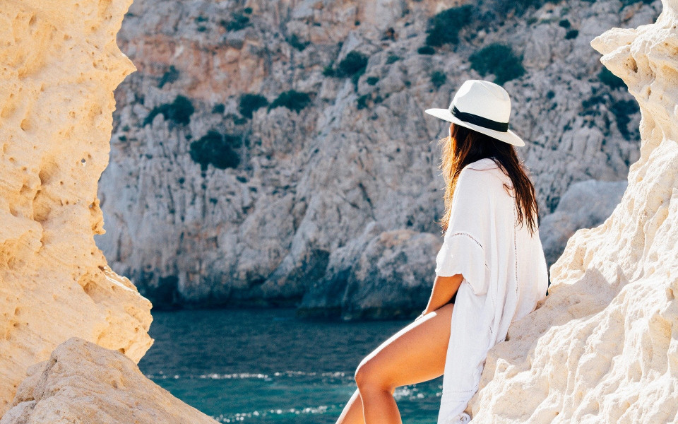Pauschalreise: Frau lehnt auf einer Klippe am Meer