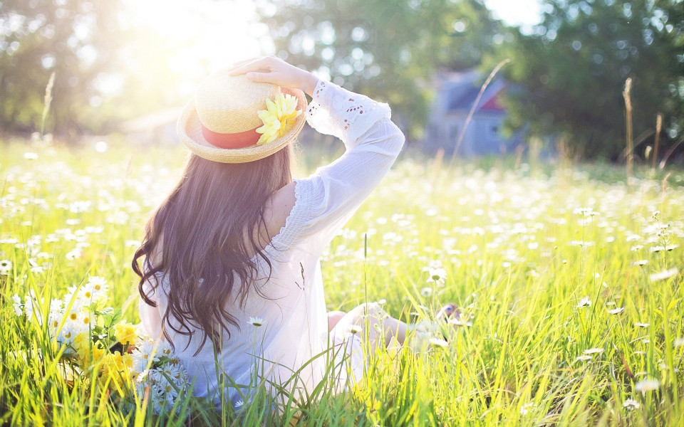 Frau sitzt in der Wiese mit Hut bei Sonnenschein