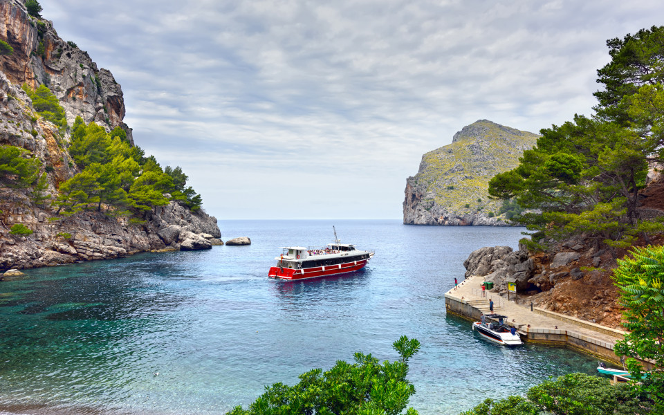  Mallorca Ausflugstipp: Malerische Bucht von Sa Calobra auf Mallorca mit kristallklarem Wasser, steilen Felsw&auml;nden und einem Boot, das am Pier anlegt.	