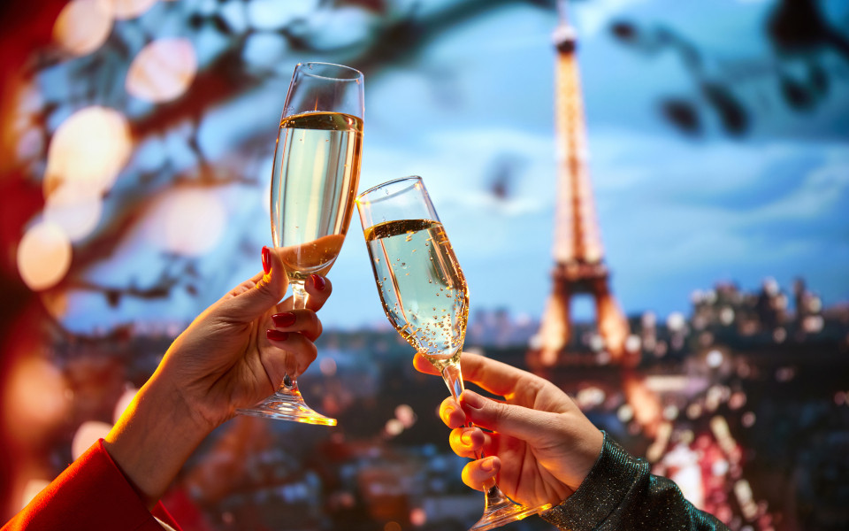 Auf der Terrasse eines feinen Restaurants in Paris mit Blick auf den Eifelturm sto&szlig;en zwei Freuen mit Champagner an
