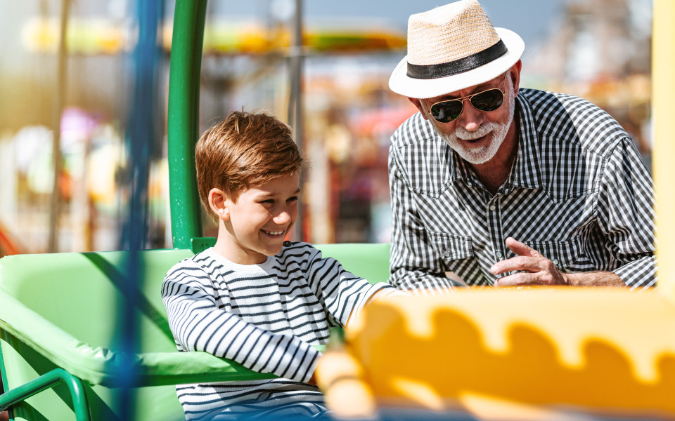 Ein Großvater und sein Enkel auf einem Fahrgeschäft im Legoland Deutschland, beide lächeln und genießen die Zeit zusammen.